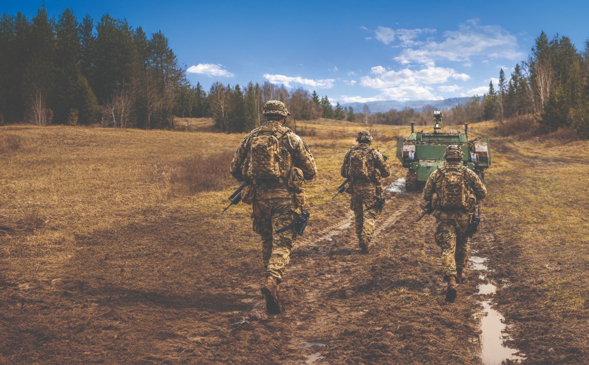 Soldiers moving with the DeMiner system across a muddy field during a defence operation
